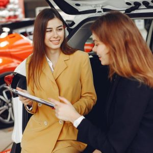 female car salesman showing contract to customer at lot