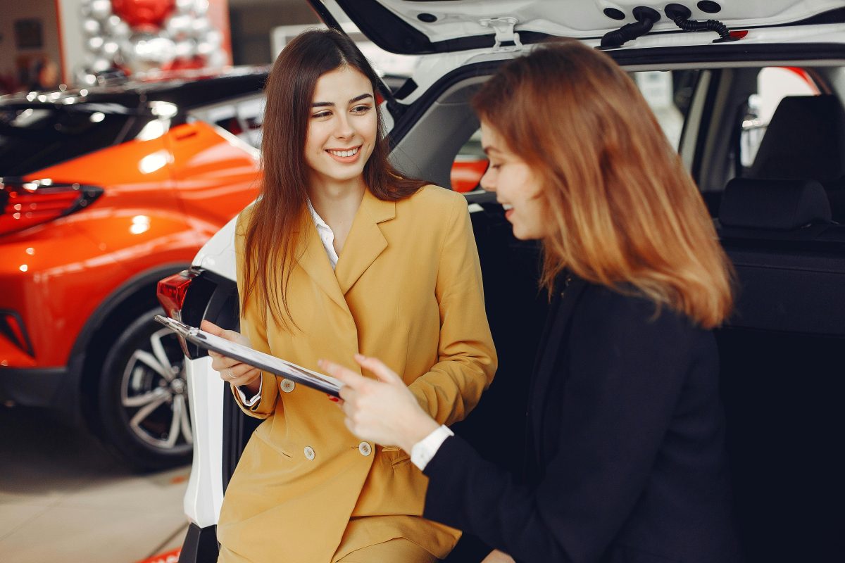 female car salesman showing contract to customer at lot