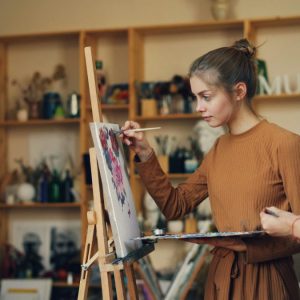 woman painting a canvas board with teacher watching