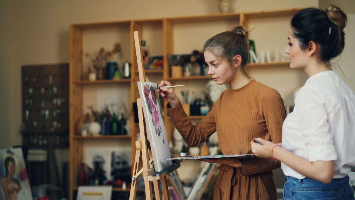woman painting a canvas board with teacher watching