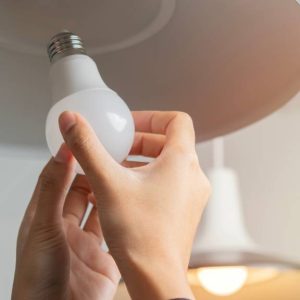 Close-up of a person's hands changing a light bulb in their home. They are using an LED bulb in the light.