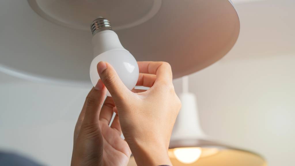 Close-up of a person's hands changing a light bulb in their home. They are using an LED bulb in the light.
