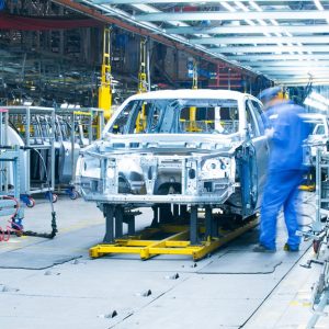 A car production line at an automotive manufacturing plant with a blue, blurred worker working on the chassis of a car.