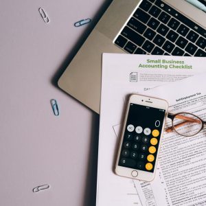 calculator, papers, and glasses sitting on a laptop with paperclips on the table