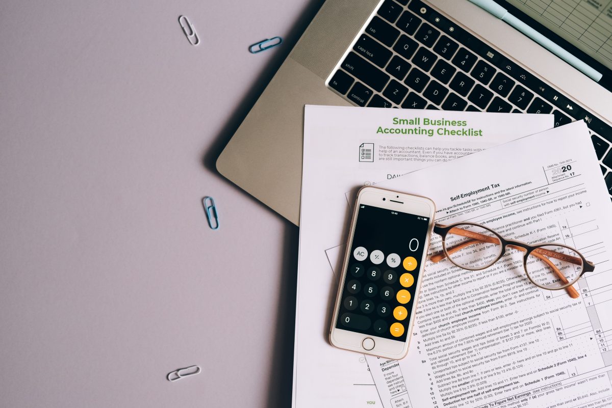 calculator, papers, and glasses sitting on a laptop with paperclips on the table