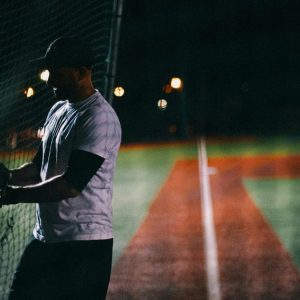 man in white t-shirt holding a bat on a baseball field