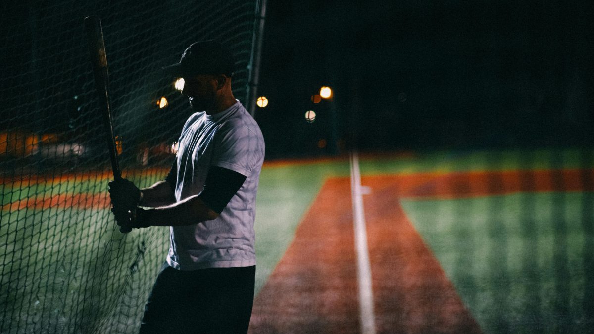man in white t-shirt holding a bat on a baseball field