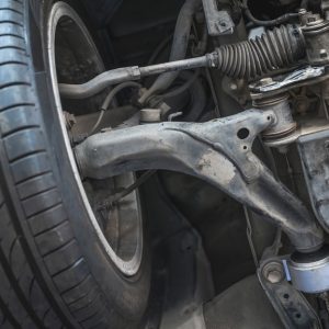 A close-up view of front suspension system components beneath a vehicle, showing metal parts and mechanical connections.