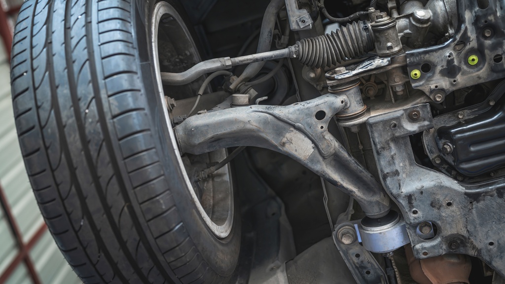 A close-up view of front suspension system components beneath a vehicle, showing metal parts and mechanical connections.