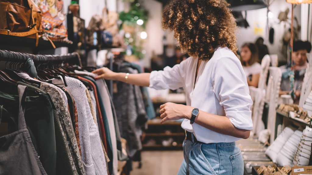 A woman browsing a clothing rack in a boutique store among curated fashion displays and accessories.