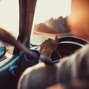 A man driving a car with one of his hands on the steering wheel while looking at the road in front of him.