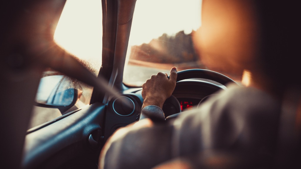 A man driving a car with one of his hands on the steering wheel while looking at the road in front of him.