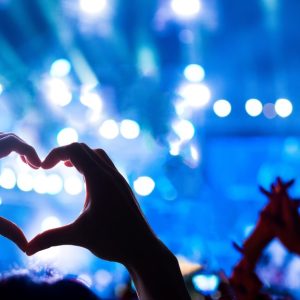 People hold up their hands while at a rock concert. One of the people makes the shape of a heart with their hands.