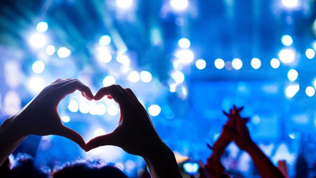 People hold up their hands while at a rock concert. One of the people makes the shape of a heart with their hands.