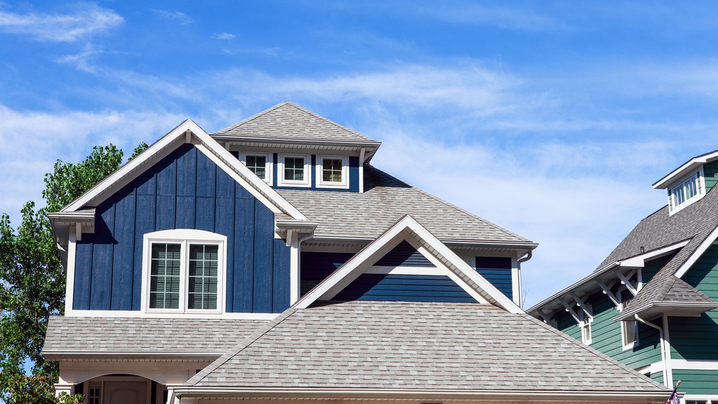 A multi-story blue beach home with a multi-tiered shingle roof with white-framed windows against a blue sky.