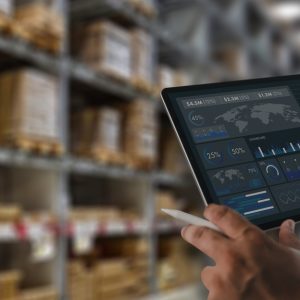 A person is standing in a warehouse while they’re holding a tablet in their hands. They have a white stylus in their hand as well.