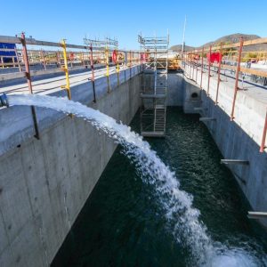 a black hose releasing water into a concrete basin with water, wooden beams, and yellow supports in the back.