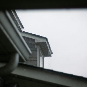 a house roof and gutter system against a grey rainy sky