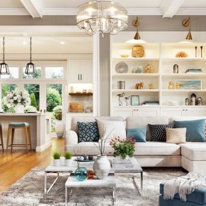 Bright open-concept living room with neutral furnishings, large windows, built-in shelving, and a connected kitchen.