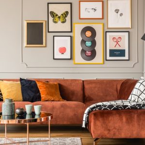 Seven pieces of artwork hanging above an L-shaped couch inside a home. The art pieces all vary in size.
