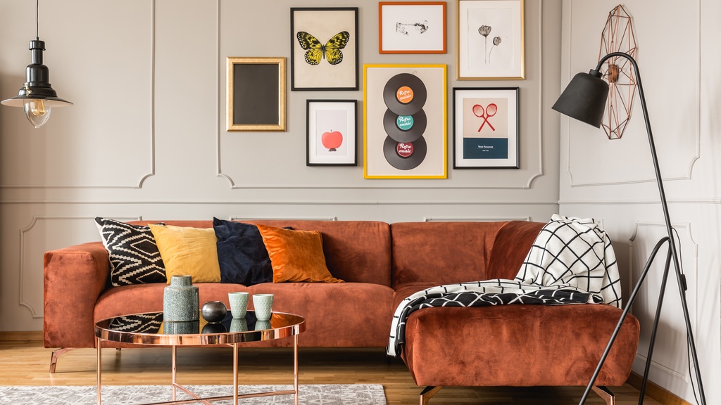 Seven pieces of artwork hanging above an L-shaped couch inside a home. The art pieces all vary in size.