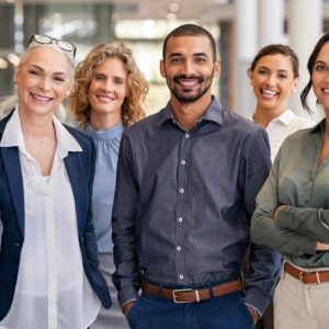 Eight professionally dressed adults of various ages standing and smiling in a brightly lit office space.
