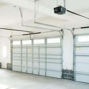 A well-lit, empty residential garage with a concrete floor, wooden steps, and two closed garage doors.