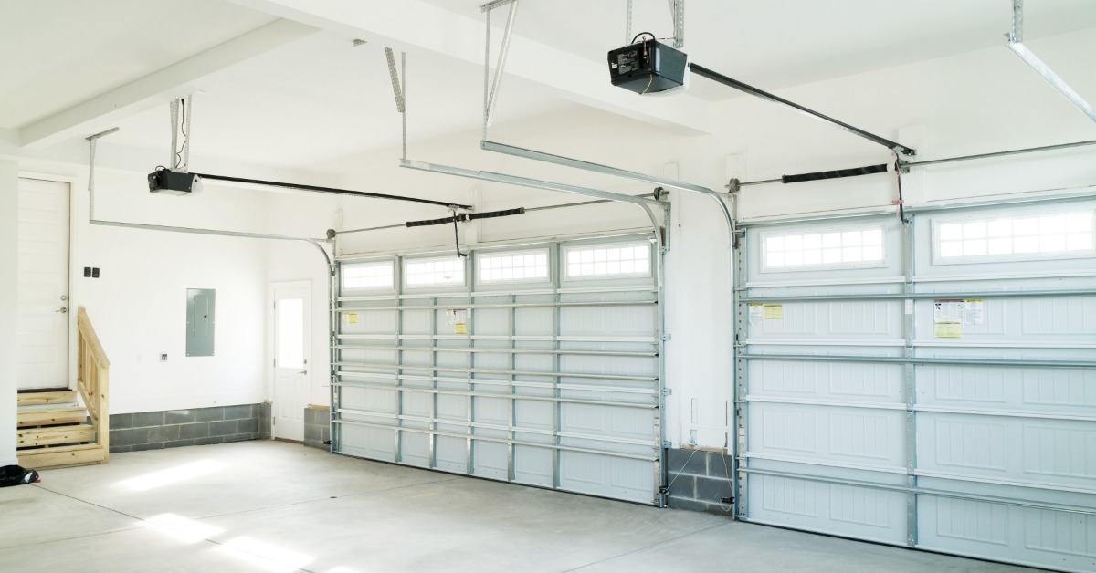 A well-lit, empty residential garage with a concrete floor, wooden steps, and two closed garage doors.
