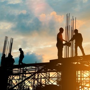 The silhouette of several construction workers working on a building under construction during the sunset.