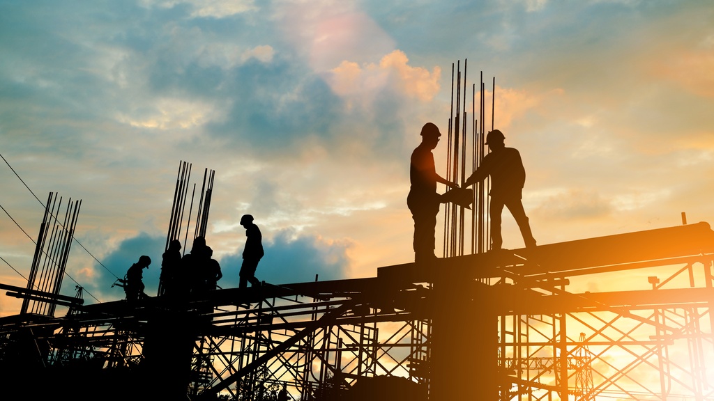 The silhouette of several construction workers working on a building under construction during the sunset.
