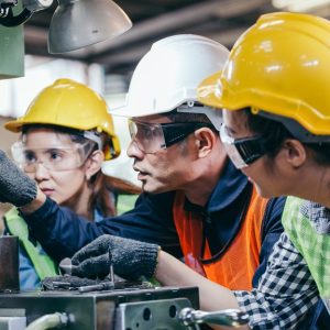 A man is pointing at a piece of industrial machinery. There are two people, one on either side of the man.