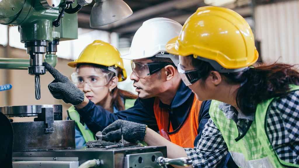 A man is pointing at a piece of industrial machinery. There are two people, one on either side of the man.