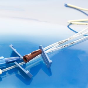 A triple-lumen central venous catheter has clear tubes and three colored ports—brown, blue, and white.