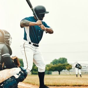 A man in a blue and white baseball jersey stands at the plate with a bat next to a catcher, awaiting the pitch.