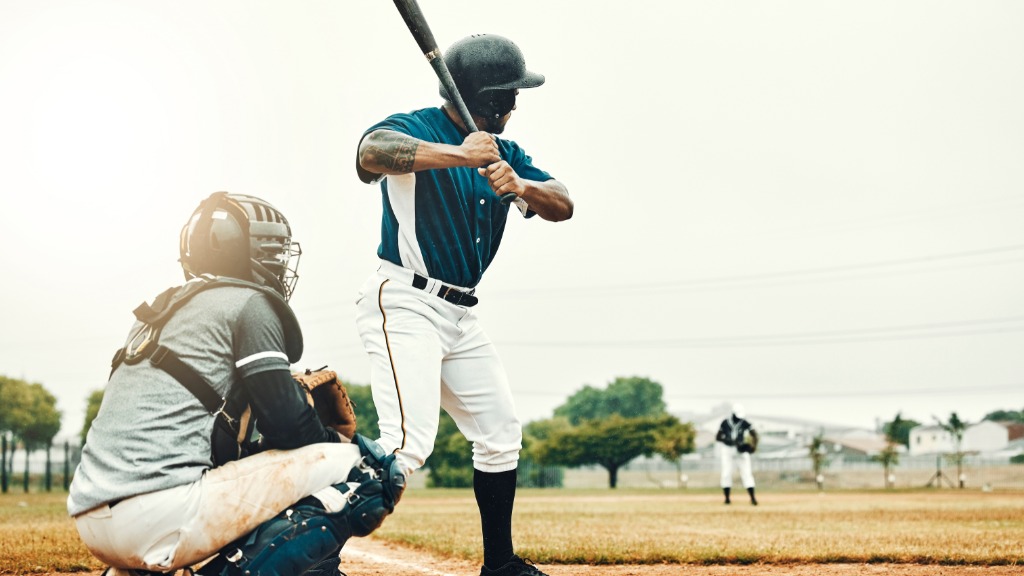 A man in a blue and white baseball jersey stands at the plate with a bat next to a catcher, awaiting the pitch.