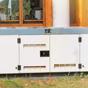 A close-up of a white diesel standby generator sitting on the grass outside a home with large white pillars.