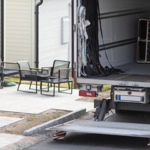 A box truck has it’s back door open. There are several items inside the truck and boxes are stacked next to it.