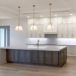 A modern kitchen with an island, white cabinets, a large window, stainless-steel appliances and wooden floors.
