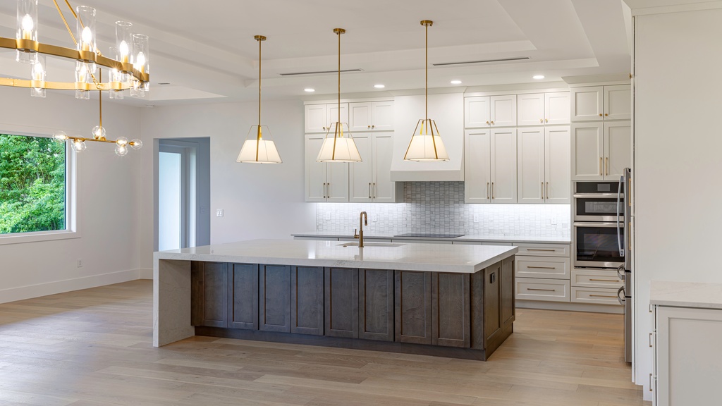 A modern kitchen with an island, white cabinets, a large window, stainless-steel appliances and wooden floors.