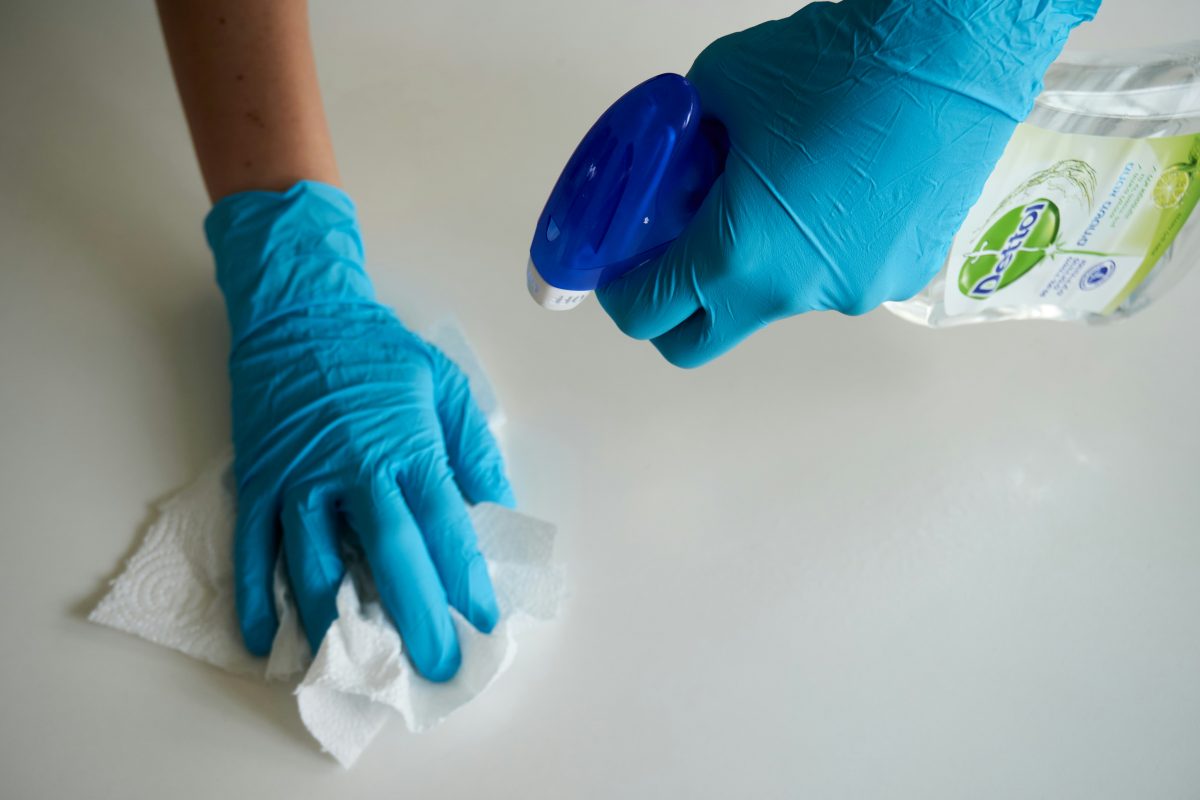 person in blue gloves cleaning a surface with spray and paper towel