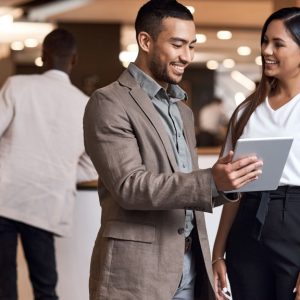 A professionally dressed person at a trade show holds a tablet in front of a guest. The duo stand by two more guests.